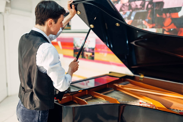 Pianista mężczyzna otwiera pokrywę czarnego fortepianu. Muzyk dostosowuje royale, klasyczny instrument muzyczny dostrajania - Zdjęcie, obraz
