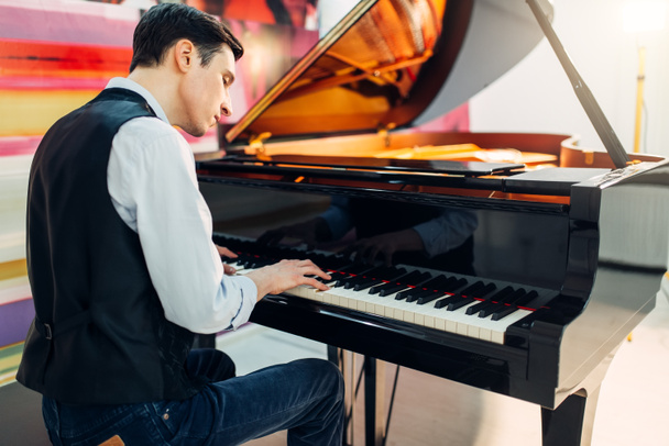 Mannelijke pianist op de klassieke zwarte vleugel, de prestaties in de studio. Muzikant speelt een melodie bij de royale toetsenbord, muziekinstrument - Foto, afbeelding