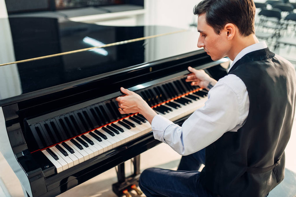 Мужчина-пианист открывает крышку клавиатуры черного рояля. Музыкант готовится к выступлению на рояле, классическом музыкальном инструменте
 - Фото, изображение