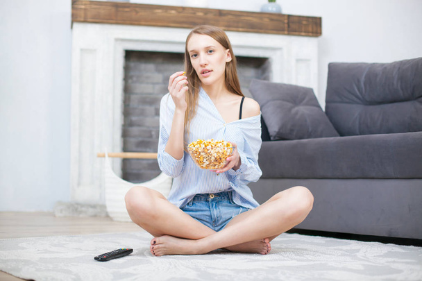 Beautiful young smiling woman watching a movie in the bed and eating popcorn - Foto, Imagen