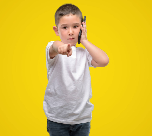 Petit enfant aux cheveux foncés utilisant un smartphone pointant du doigt vers la caméra et vers vous, signe de la main, geste positif et confiant de l'avant
 - Photo, image