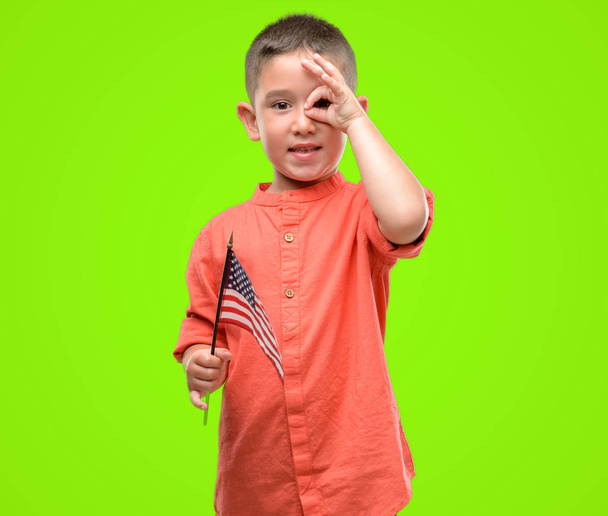 Dark haired little child holding United States flag with happy face smiling doing ok sign with hand on eye looking through fingers - Φωτογραφία, εικόνα