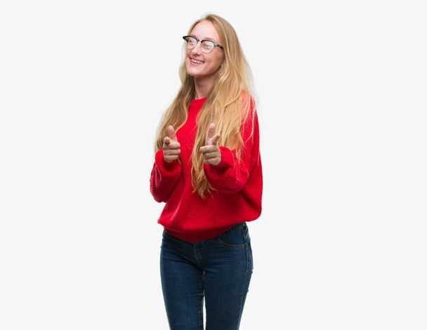 Блондинка-підліток в червоному светрі вказує пальці на камеру з щасливим і смішним обличчям. Хороша енергія і вібрує
. - Фото, зображення