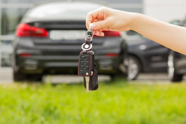 hand of a girl with a car key in her hand, against a new car background - Photo, Image