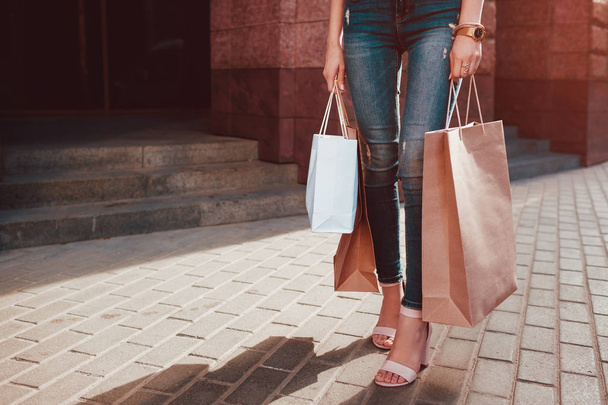 junge Frau mit Einkaufstaschen, die im Sommer auf der Straße läuft. Nahaufnahme der Hände mit Einkäufen und Absätzen. Verkauf. Schwarzer Freitag - Foto, Bild