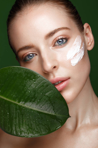 Beautiful fresh girl with cosmetic cream on the face, natural make-up and green leaves. Beauty face. - Foto, Imagen