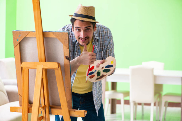 Jonge mannelijke kunstenaar werkt aan nieuw schilderij in zijn atelier - Foto, afbeelding