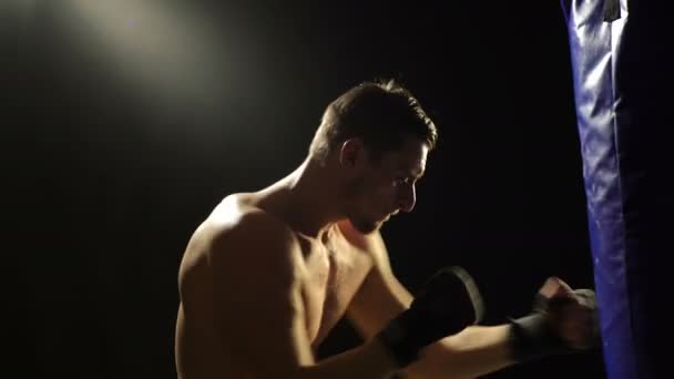 Boxing concept. A boxer trains on a blue pear isolated on a black background. Strong boxer on a black background. - Filmati, video