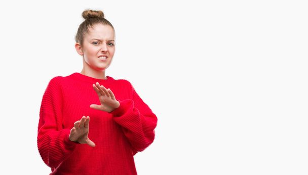 パンと赤いセーターを身に着けている若いブロンドの女性はうんざり表現で、不快と恐ろしいので嫌悪顔をやって嫌悪反応。手で発生します。迷惑な概念. - 写真・画像