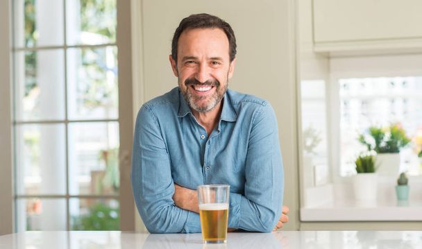 Średnim wieku człowiek picia piwa z szczęśliwy twarz stałego i uśmiechając się z uśmiechem pewnie Wyświetlono zębów - Zdjęcie, obraz