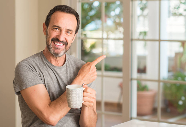 Чоловік середнього віку п'є каву в чашці дуже щасливий вказуючи рукою і пальцем в сторону
 - Фото, зображення