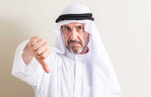 Homem árabe sênior com cara zangada, sinal negativo mostrando antipatia com os polegares para baixo, conceito de rejeição
 - Foto, Imagem