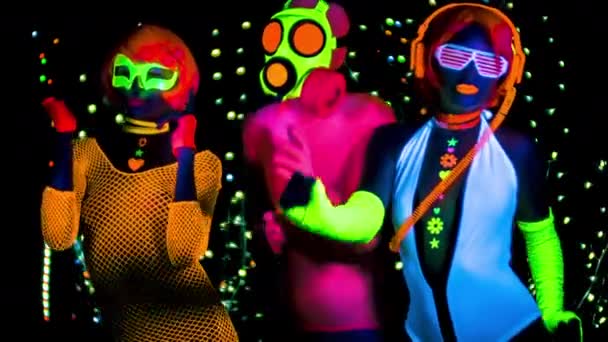 Naiset ja mies kaasunaamarissa loistevaatteissa UV-mustassa valossa
 - Materiaali, video