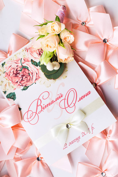 Ένα κοντινό πλάνο του μια γαμήλια πρόσκληση και μια μπουτονιέρα για τον γαμπρό στο φόντο των ροζ τόξα - Φωτογραφία, εικόνα