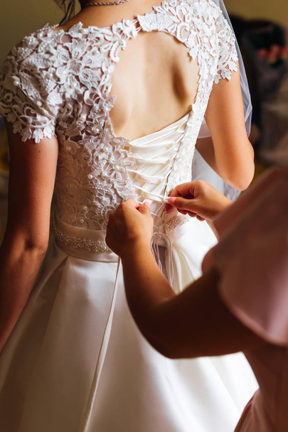 primer plano de la novia de la novia que ayuda a la novia a vestir su vestido de novia con un encaje y una cinta en el corsé
 - Foto, Imagen