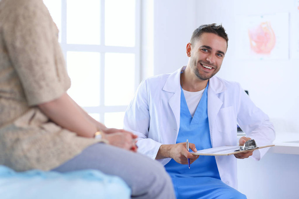 Handsome doctor is talking with young female patient and making notes while sitting in his office - Foto, imagen