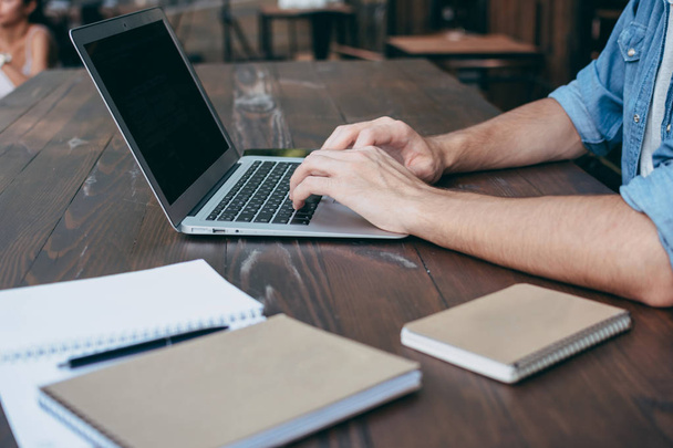 Męskie ręce są drukowane na laptopie na drewnianym stole brązowy w kawiarnię, bezpłatne Wi-Fi, na pierwszym planie notebook. Koncepcja freelancer działa zawsze, gdziekolwiek. Widok z boku, koncepcja - Zdjęcie, obraz