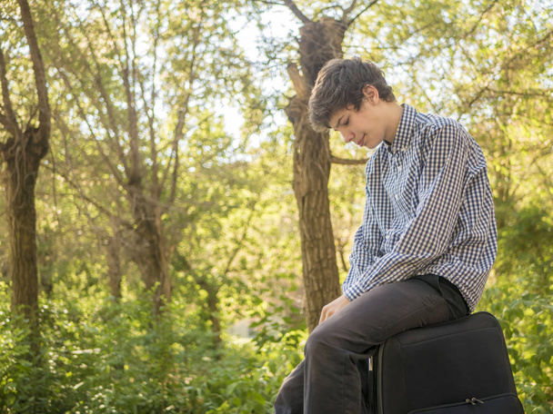大きな荷物ケース バッグ屋外夏の街の上に座って疲れた若い 10 代男 - 写真・画像