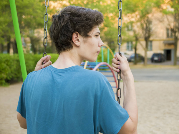 close up back portrait of young teenager sit on a swing on a children playing ground - Photo, Image