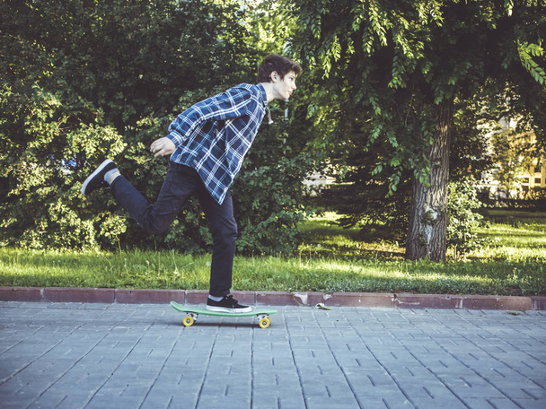 young hipster riding a penny board skateboard in the summer city street - Фото, изображение
