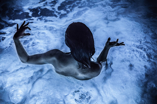 Girl is making weird finger symbols while swimming in a jacuzzi with blue light - Foto, Imagem
