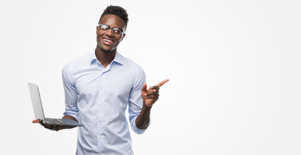 Nuori afrikkalainen amerikkalainen liikemies tietokoneella kannettava erittäin onnellinen osoittaa käsin ja sormella sivulle
 - Valokuva, kuva