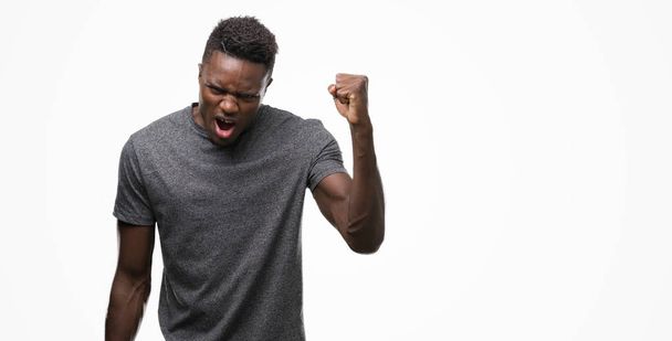 Fiatal afroamerikai férfi mérges és őrült emelése a csalódott és dühös, miközben kiabált a harag ökle szürke pólót visel. Düh és agresszív koncepció. - Fotó, kép