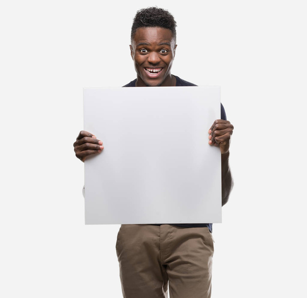 Young african american man holding a banner screaming proud and celebrating victory and success very excited, cheering emotion - Фото, изображение