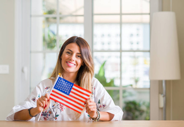 Giovane donna a casa che tiene la bandiera degli Stati Uniti d'America con un viso felice in piedi e sorridente con un sorriso fiducioso che mostra i denti
 - Foto, immagini