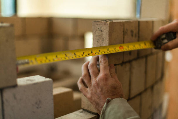 Brickmason tenant un ruban à mesurer pour calculer la distance entre deux briques lors de la construction d'un mur de briques rondes
 - Photo, image