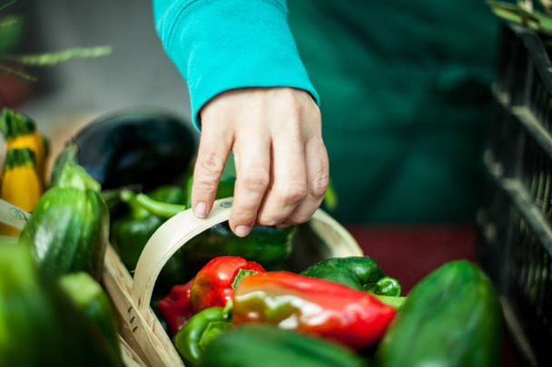Vrouw oppakken van een mandje van groene en rode paprika's op de boerenmarkt - Foto, afbeelding
