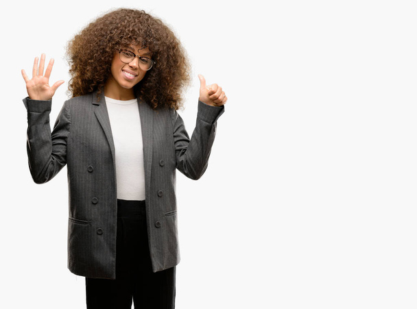 Mujer de negocios afroamericana con gafas mostrando y apuntando hacia arriba con los dedos número seis mientras sonríe confiada y feliz
. - Foto, Imagen