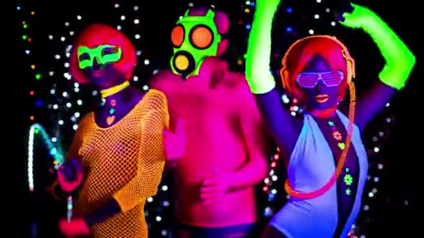 Women and guy in gas mask in fluorescent clothing under UV black light - Footage, Video
