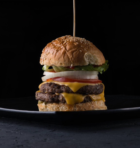 juicy cheeseburger on a plate on a black background, close - up - Zdjęcie, obraz