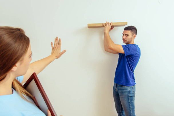 Young woman showing to boyfriend for hanging shelf on wall at home - Fotografie, Obrázek