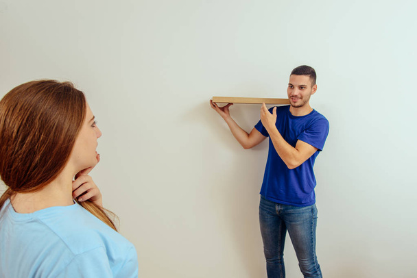 Young man trying to put shelf on the wall in their living room - Φωτογραφία, εικόνα
