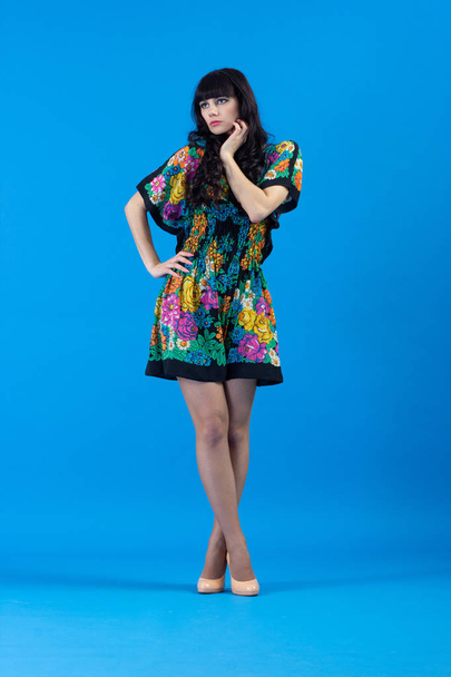 Γυναίκα όμορφη νεαρή μόδας πολύχρωμο φόρεμα Flirty ποζάρουν σε μπλε φόντο. - Φωτογραφία, εικόνα