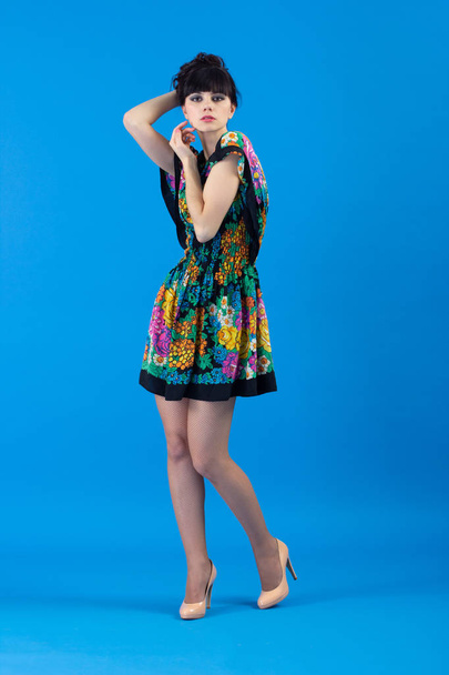 schöne junge Modefrau in buntem Kleid flirty posiert auf blauem Hintergrund. - Foto, Bild