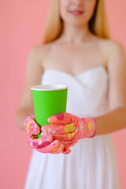 Ragazza che indossa guanti mantenendo vetro verde con tè in sfondo monofonico rosa
. - Foto, immagini