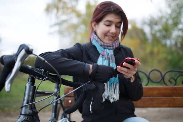 Photo of smiling woman looking in phone sitting on bench - Foto, Bild