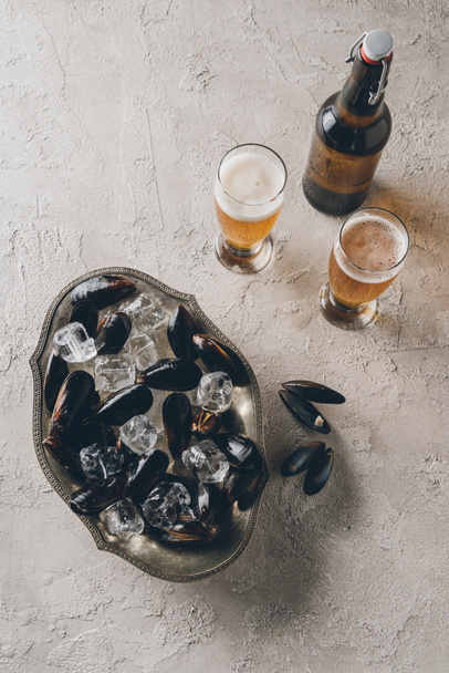 top view of mussels in bowl, glasses and bottle of beer on concrete surface - Foto, Bild