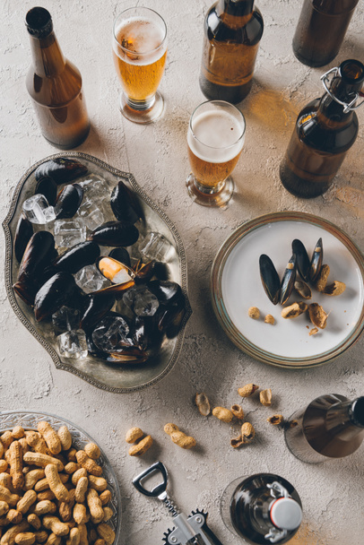 bovenaanzicht van pinda's, mosselen met ijsblokjes en een koud biertje gerangschikt op betonnen tafelblad - Foto, afbeelding