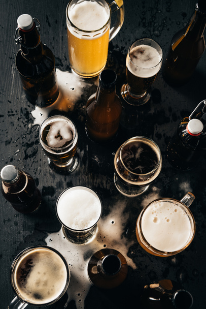 top view of arrangement of bottles and glasses of beer on dark wooden tabletop - 写真・画像