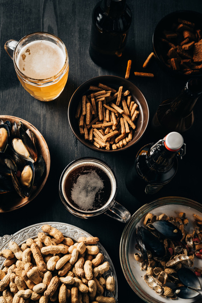 Ansicht des mit Snacks und Bier gedeckten Tisches auf dunkler Holzoberfläche - Foto, Bild