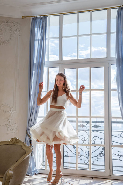 Fashion shot of beautiful blonde woman in white dress standing against white interior background - Fotografie, Obrázek