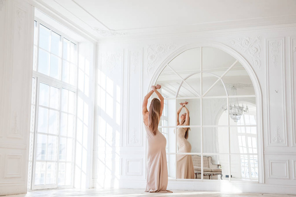 Fashion shot of beautiful blonde woman in beige dress standing against white interior background - Fotoğraf, Görsel