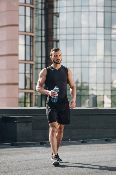 handsome sportsman walking with sport bottle of water on roof - Photo, image