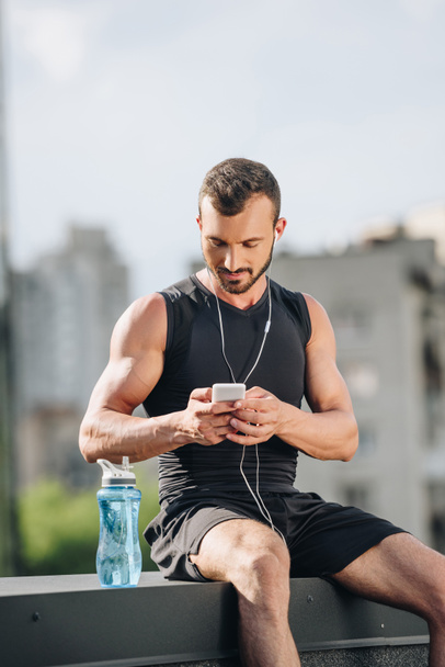 handsome sportsman listening music and using smartphone on roof  - Fotó, kép