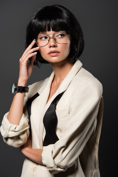 atractiva joven en chaqueta elegante y gafas mirando hacia otro lado aislado en gris
 - Foto, Imagen