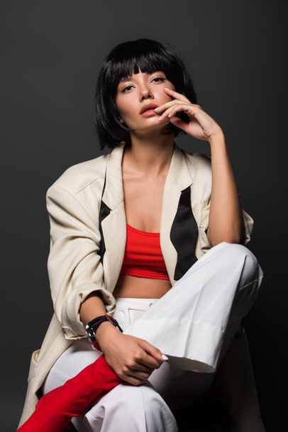 seductive young woman in stylish jacket sitting on chair isolated on grey - Foto, Imagen